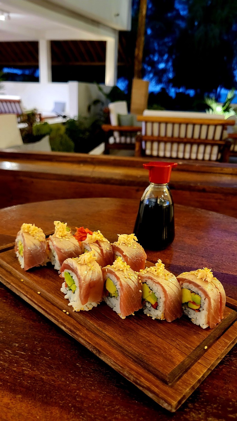 Tuna-topped roll with sesame beside a soy bottle at dusk on the terrace