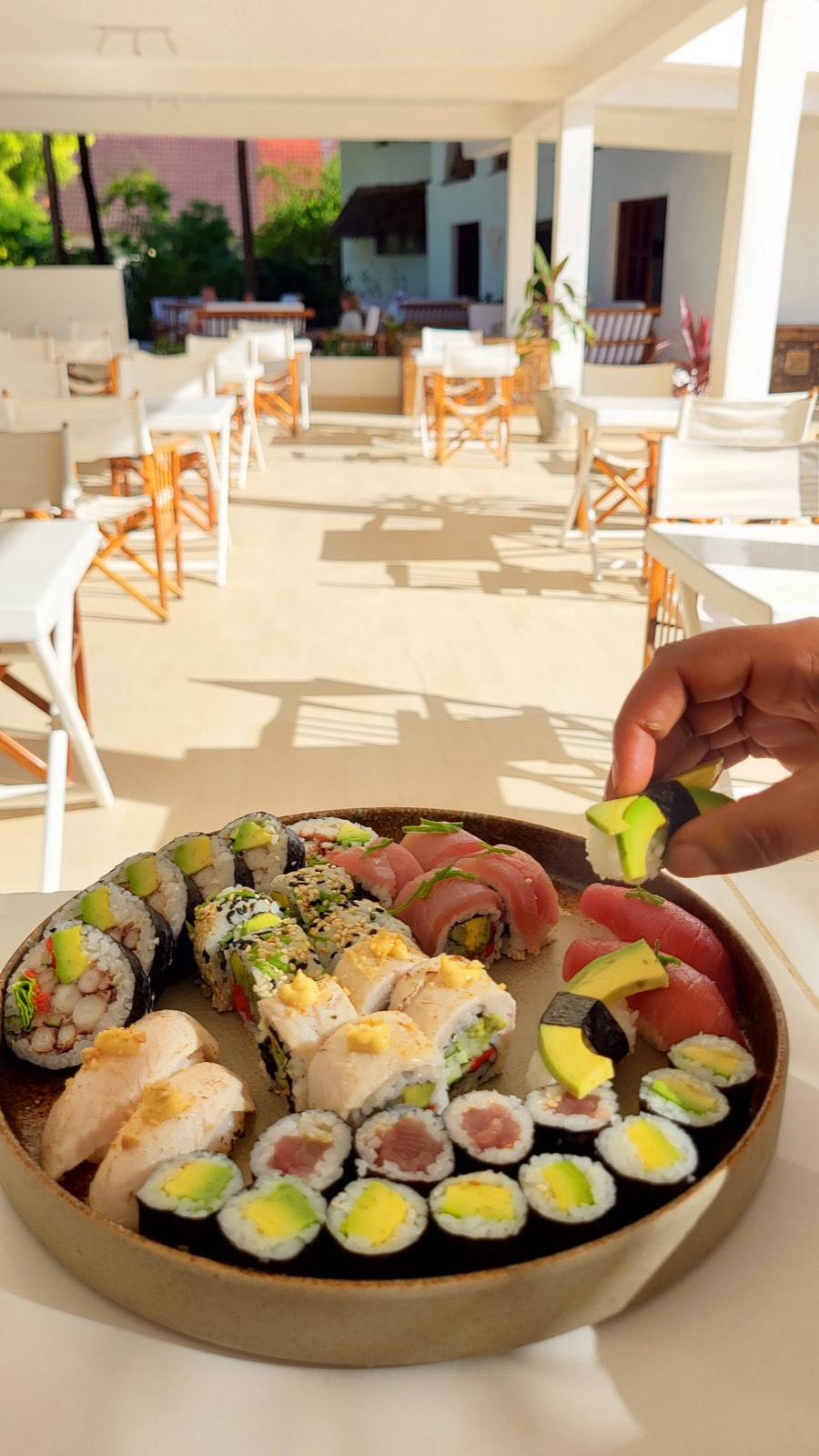 A hand lifting a piece of sushi from a platter on KAMI's sunlit terrace