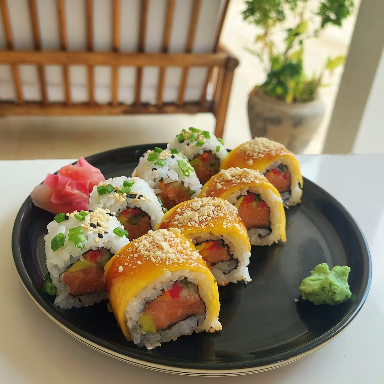 Mango-draped salmon rolls with pickled ginger and wasabi on a black plate